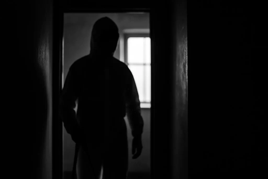 Silhouette floue d'un nettoyeur en combinaison à l'entrée d'une pièce sombre, lumière de fenêtre visible