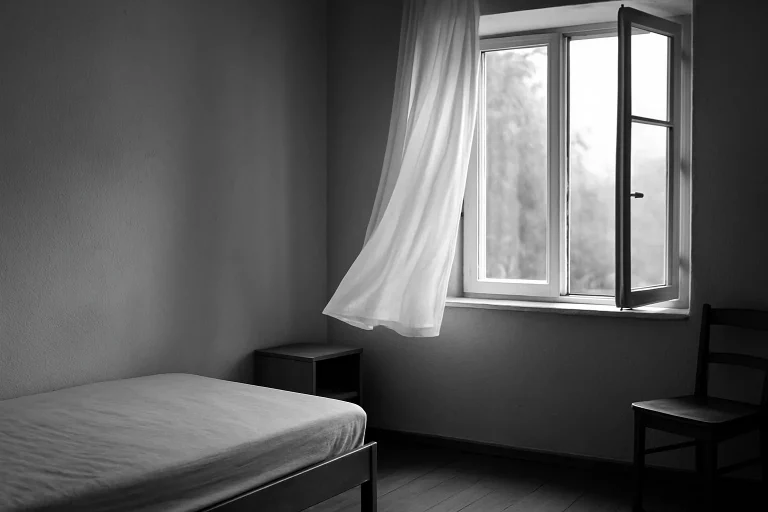 Chambre vide avec fenêtre ouverte et rideaux flottants, lumière extérieure.