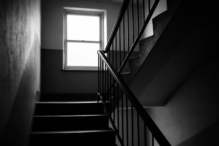 Cage d'escalier en noir et blanc dans un immeuble de Verdun, balustrade en métal et lumière naturelle.
